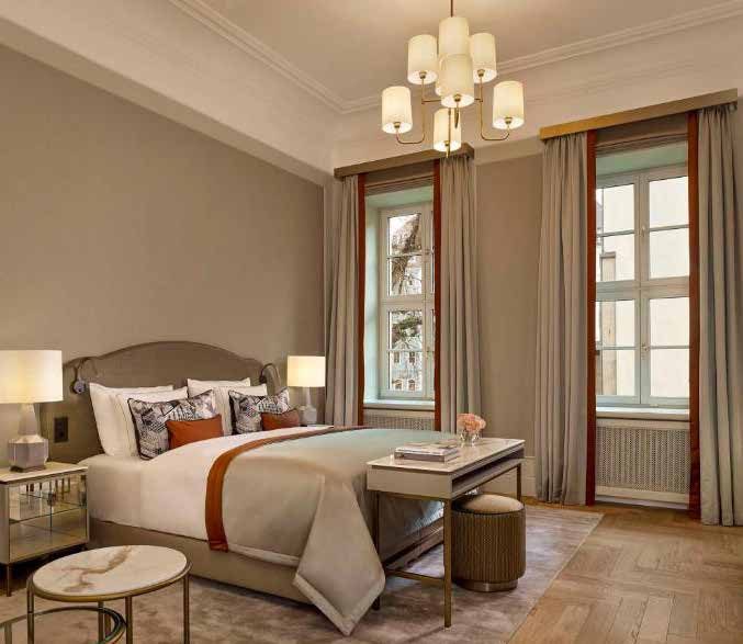 Zimmer im Designtyp I: gepolstertes Bett mit heller Tagesdecke und rostrotem Streifen, Messing-Kronleuchter, hohe Fenster mit Vorhängen und Fischgrätparkett