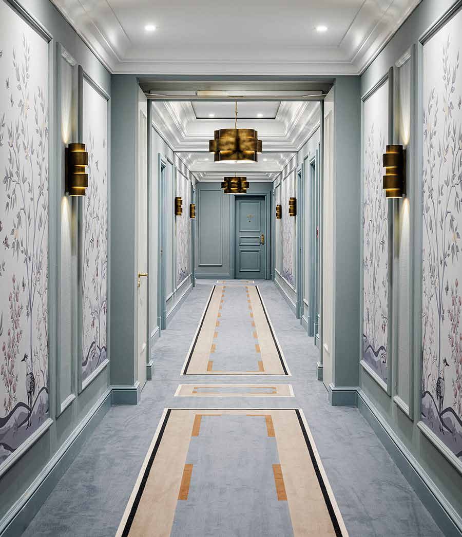 Hotelflur nach der Sanierung: blaugraue Wandfelder mit floraler Bildtapete, Messingleuchten und Teppich mit hellem Längsmuster