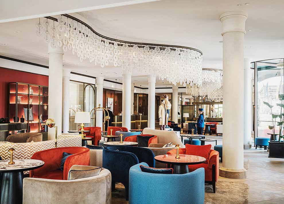 Die Lobby heute: geschwungener Glasleuchter über Sitzgruppen mit roten, blauen und beigen Sesseln zwischen weißen Säulen