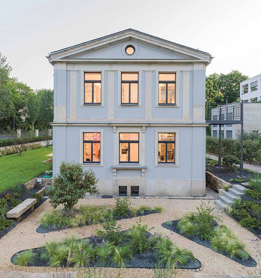 Nachher: symmetrische Giebelfassade mit erleuchteten Fenstern, davor der neu angelegte Garten mit geschwungenen Beeten
