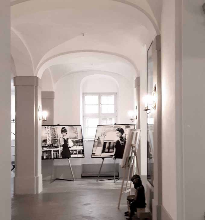 Der Raum der Patisserie vor der Sanierung: weiß verputzter Gewölbegang mit Pfeilern und einer Fotoausstellung auf Staffeleien