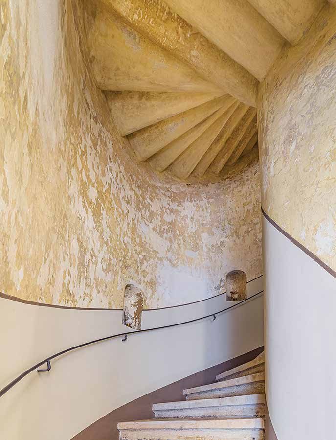 Blick in das historische Treppenhaus: steinerne Wendeltreppe mit Handlauf an der geschwungenen, patinierten Wand